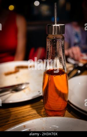 Eine würzige Flasche Olivenöl, gemischt mit getrocknetem rotem Pfeffer und den Überresten der Pizzen, sitzt auf einem Tisch in Hiroshima, Japan. Stockfoto