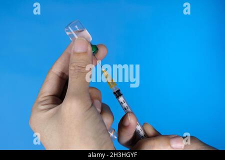 Eine Nahaufnahme der Hände des Arztes mit einer Spritze und einer Flasche Impfstoff. Klare Glas-Impfstoffflasche. Blauer Hintergrund. Healthcare und Medical Konzept. Stockfoto
