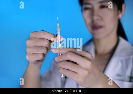 Eine asiatische Ärztin hält eine Spritze mit Covid-19-Impfstoff in die Hand und misst die Dosierung, bevor sie sie ihrem Patienten injiziert. Stockfoto