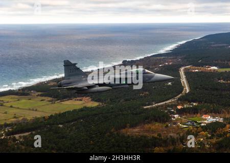 Ein schwedischer Saab JAS 39 Gripen-Kampfjet begleitet eine angesehene Besucherparty an Bord einer schwedischen C-130H über Gotland, Schweden, 23. Oktober 2021. Die herausragenden Besucher besichtigten die Insel im Rahmen eines von Schweden geführten bilateralen Engagements, zu dem auch eine Demonstration des HIMARS (High Mobility Artillery Rocket System) der Wisconsin Army National Guard gehörte, bei der die fortgesetzten Bemühungen der USA und Schwedens zur Aufrechterhaltung der Interoperabilität und der schnellen Reaktionsbereitschaft in der Region demonstriert wurden. (USA Army Photo von Sgt. Patrik Orcutt) Stockfoto