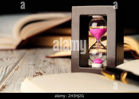 Sandglas auf Holztisch mit geöffnetem Buch aus nächster Nähe Stockfoto