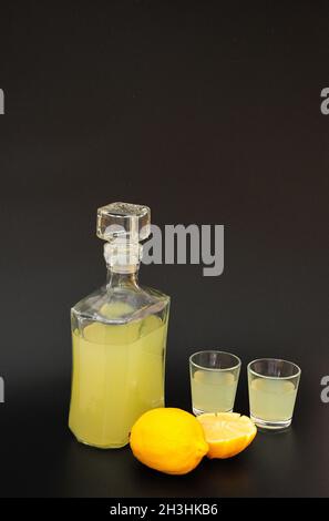 Zitronenlikör, starker Alkohol in Gläsern und eine Glasdekanter auf schwarzem Hintergrund, neben reifen Zitrusstücken. Nahaufnahme. Stockfoto