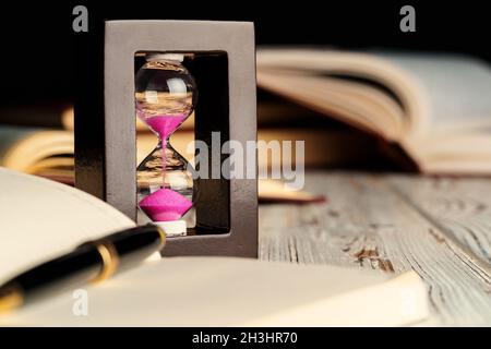 Sandglas auf Holztisch mit geöffnetem Buch aus nächster Nähe Stockfoto