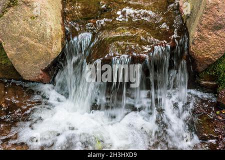 Ein kleiner Wasserfall in der Sommerhitze im Stadtpark. Wasser fließt über die Steine Stockfoto