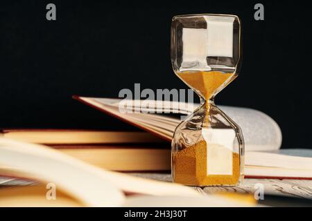 Sandglas auf Holztisch mit geöffnetem Buch aus nächster Nähe Stockfoto