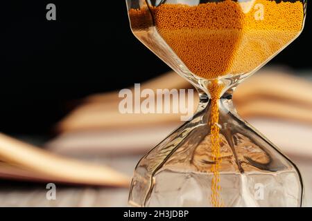 Sandglas auf Holztisch mit geöffnetem Buch aus nächster Nähe Stockfoto