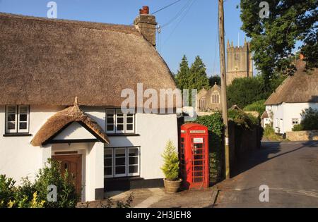 Strohgedeckte Hütten, einschließlich der alten Post, der roten Telefondose und der Kirche kurz nach Sonnenaufgang in North Bovey, Dartmoor National Park, Devon Stockfoto