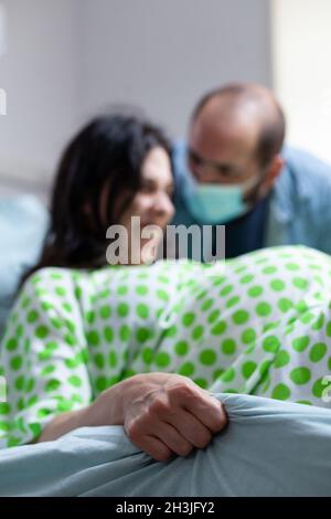 Nahaufnahme einer Frau, die das Bettlaken mit der Hand hält, während sie gebiert und schmerzhafte Kontraktionen auf der Krankenstation hat. Person in der Kindergeburten Druck und Ehemann bei der Mutterschaft zu helfen Stockfoto