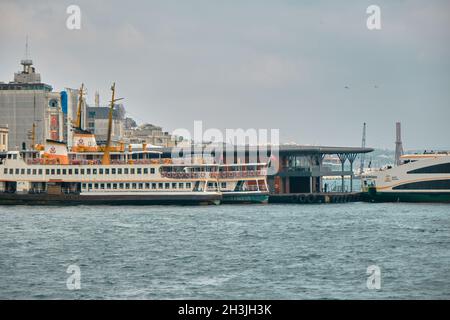 Karakoy Küste von istanbul und viele Fußgängerfähre in goldenem Horn mit kleinem Fischerboot während bewölktem und regnerischem Tag in istanbul verankert. Stockfoto