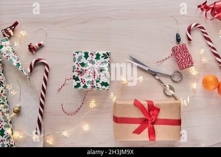 Weihnachtskomposition. Geschenkschachteln, Geschenkverpackungen mit Papier und Band, Lichter, Süßigkeiten Stöcke auf Holz Hintergrund. Holdiay DIY handgemachte Haus dekorat Stockfoto