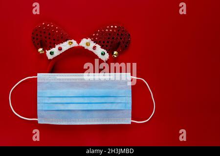 Festliche Coronavirus-Elfe aus Gesichtsmaske und Dekorationen auf rotem Hintergrund. Flat Lay, Draufsicht weihnachtsfeiertage Komposition. Neujahr Tapete BA Stockfoto