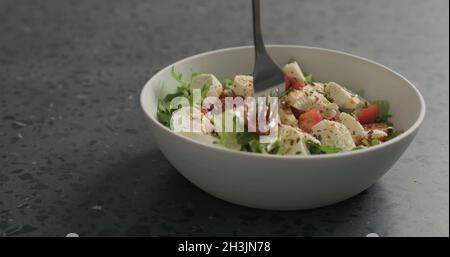 Man handpflücken Salat mit Mozzarella, Kirschtomaten und Friseeblättern in weißer Schüssel auf Terrazzooberfläche, breites Foto Stockfoto