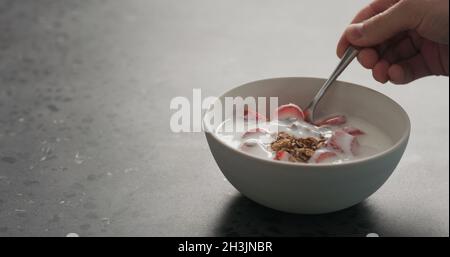 Mann Hand essen Schokolade Müsli mit Erdbeeren und Joghurt auf einer Betonplatte, breites Foto Stockfoto