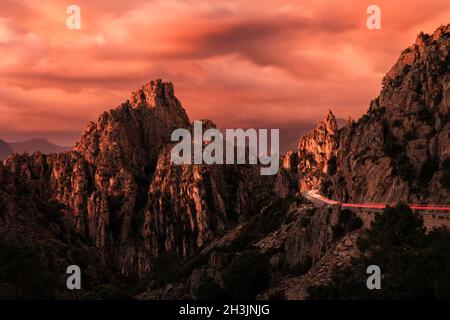 Rote Ampelwege auf der D81 Straße, die sich bei Sonnenuntergang durch die dramatischen Felsformationen der Calanches of Piana schlängelt, die zum UNESCO-Weltkulturerbe gehören Stockfoto