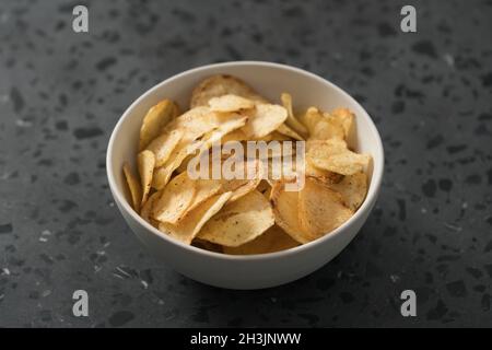 Kartoffelchip leicht mit schwarzem Pfeffer in weißer Schüssel auf Beton Hintergrund, flacher Fokus bestreut Stockfoto