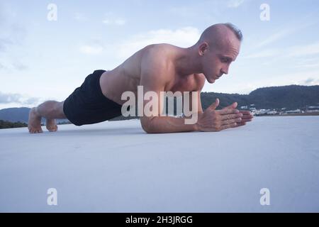 Schöner, muskulöser Mann, der auf einem Dach über dem blauen Himmel Plankenposition einnimmt Stockfoto