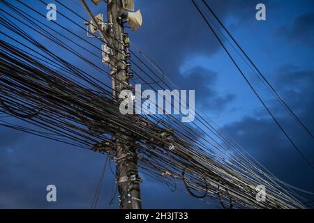 Chaos von Kabeln und Drähten auf dem Strommast über dem Abendhimmel Stockfoto