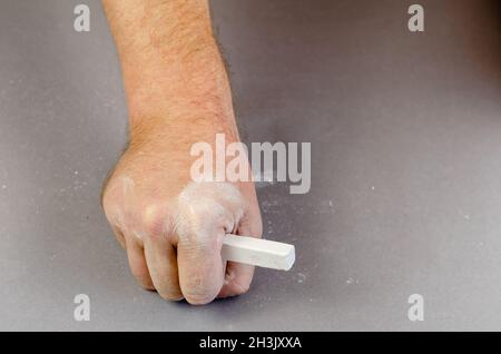 Die Hand eines erwachsenen Mannes hält ein Stück weiße Kreide. Selektiver Fokus. Stockfoto
