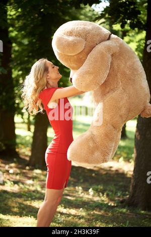 Glückliche junge Frau mit einem riesigen Teddybären im Park. Stockfoto