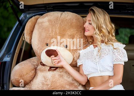 Glückliche junge Frau mit einem riesigen Teddybären im Auto. Stockfoto