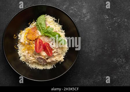 Pasta mit Fleischkäse und Basilikum auf einem schwarzen Teller Stockfoto