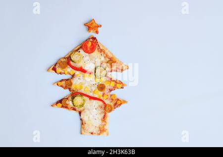 Leckere vegetarische Weihnachtsbaum-Pizza mit Tomaten, Gemüse und Käse auf blauem Hintergrund. Kreatives, witziges Food-Konzept für Kinder. Draufsicht Stockfoto