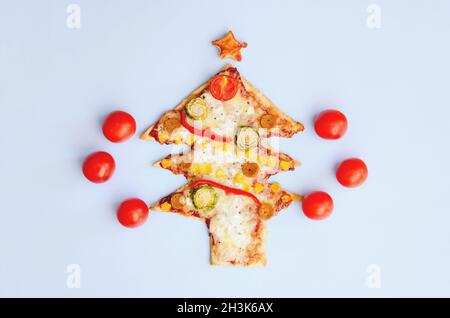 Leckere vegetarische Weihnachtsbaum-Pizza mit Tomaten, Gemüse und Käse auf blauem Hintergrund. Kreatives, witziges Food-Konzept für Kinder. Draufsicht Stockfoto