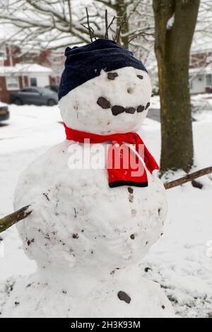 Nahaufnahme eines großen Schneemanns, der von Kindern mit schwarzem Hut und rotem Schal gebaut wurde. Zwei große Schneebälle, mit Zweigen für Arme und Steinen für Augen und Smiley Stockfoto