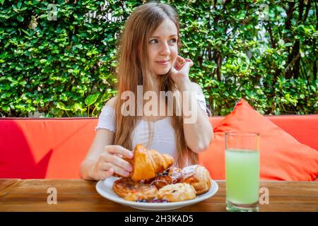 Glückliche Frau essen süßes Frühstück oder Mittagessen im Restaurant im Freien, frisches Gebäck Stockfoto