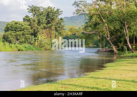 Seilschaukel hängend von einem Baum über einem fließenden Fluss in einer Naturparkumgebung in Thailand mit üppigem grünem Laub und morgendlichen Herbstblättern. Stockfoto