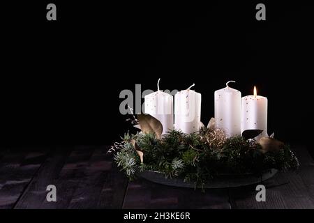 Erster Advent - Adventskranz aus Tanne und immergrünen Ästen mit weißen brennenden Kerzen auf dunklem Holztisch. Tradition in der Zeit vor Weihnachten. Stockfoto