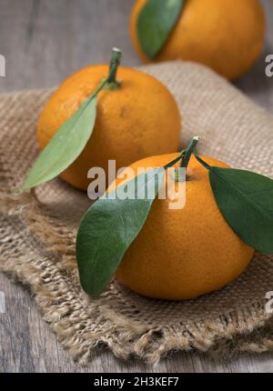 Frische reife Mandarinen mit Blättern in einer Schüssel auf einem hölzernen Hintergrund. Stockfoto