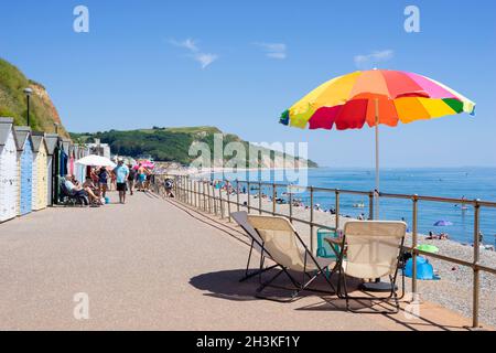 Seaton Devon sonnt sich und nutzt Sonnenschirme an den Strandhütten entlang der Promenade am Seaton Devon England GB Europe Stockfoto