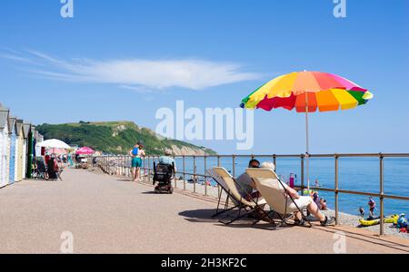 Seaton Devon sonnt sich und nutzt Sonnenschirme an den Strandhütten entlang der Promenade am Seaton Devon England GB Europe Stockfoto