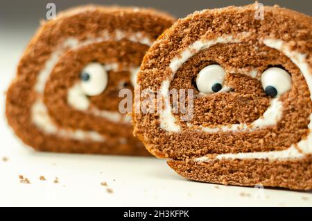Schokoladen-Biskuitrolle mit Vanillegeschmack, Füllung mit dekorieren süßen Augen, Schokolade schweizer Rolle, lustiges Essen Stockfoto