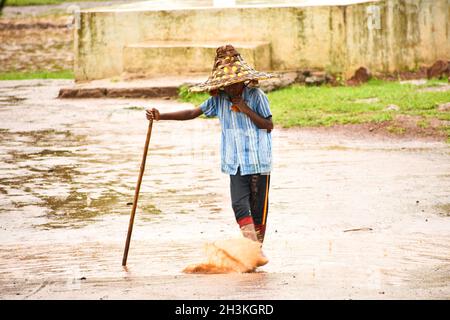 SURAJPUR, INDIEN - 01. Apr 2019: Ein kleiner Dorfjunge in einem Strohhut mitten auf der Straße, der während des Regens mit Wasser spielt Stockfoto
