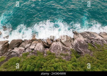 Luftaufnahme der wunderschönen Wellen des Ozeans und der felsigen Küste mit viel Grün Stockfoto