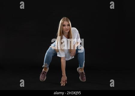 Junge Tänzerin auf gebogenen Beinen, sich mit einer Hand aufstützen und auf die Kamera schauen. Lange blonde Haare. Stockfoto