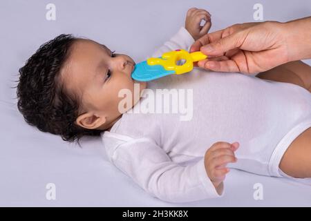 Kleinkind liegt auf dem Rücken und eine Hand legt ein Spielzeug in den Mund Stockfoto