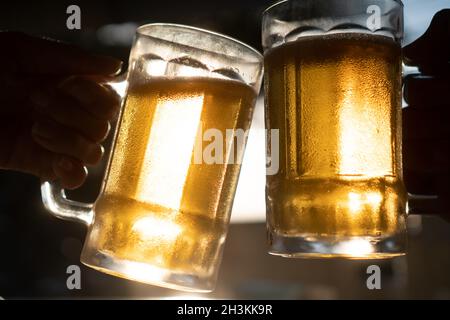 Nahaufnahme Toast klirrende frische Bierbecher mit Sonnenstrahlen an heißen Sommertagen Stockfoto