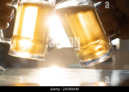 Nahaufnahme Toast klirrende frische Bierbecher mit Sonnenstrahlen an heißen Sommertagen Stockfoto