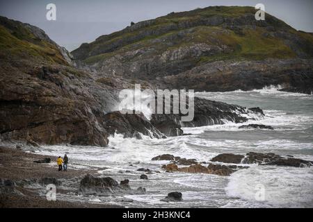 Swansea, Wales. 28. Oktober 2021, UK Wetter zwei Menschen genießen einen Strandspaziergang an der Bracelet Bay in Mumbles, während an einem nassen und windigen Tag in Südwales Wellen gegen die Felsen krachen. Stockfoto