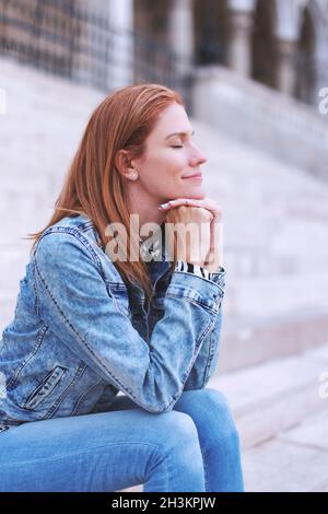 Kaukasische Rothaarige Frau, die sich auf Treppen in der Stadt im Freien ausruht Stockfoto