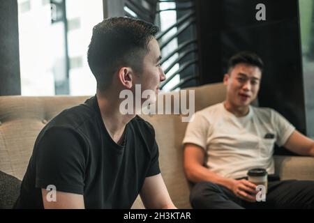 Zwei asiatische junge Männer sitzen im Café, trinken Kaffee, reden. Gruppe junger Menschen, die Spaß haben, das Leben der Millennials, den Lebensstil in der Großstadt Stockfoto