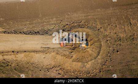 Luftaufnahme des Baggers gießt Sand in den LKW. Auf der Baustelle Draufsicht. Schießen von der Drohne. Stockfoto