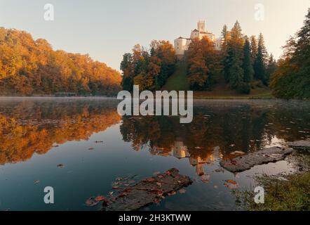 Schöne herbstliche Landschaft der Burg Trakošćan auf dem Hügel am See mit herbstlichen bunten Bäumen im Wasser in Kroatien, Grafschaft hrvatsko zagorje reflektiert umgeben Stockfoto