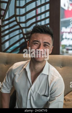 Porträt eines jungen, hübschen asiatischen Mannes in schwarzem Hemd, der im Café sitzt und lächelt. Schönes Lächeln, glückliche Person, Millennials Leben, Lebensstil Stockfoto