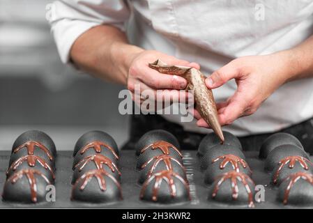 Herstellung von handgefertigten Pralinen. Ein Konditor gießt flüssige dunkle Schokolade in Formen. Nahaufnahme. Stockfoto