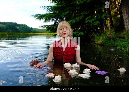 Attraktive junge Frau im Wasser mit Blumen Stockfoto