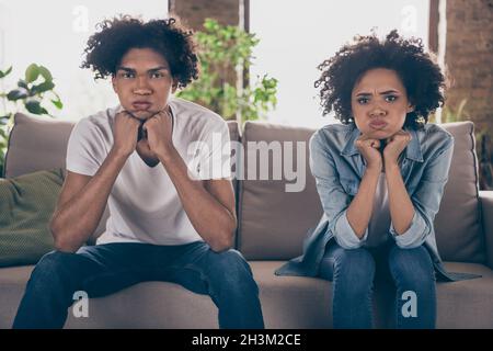 Fotoporträt Junges Paar, das auf der Couch saß, beleidigte unglücklich und hielt Atem in den Wangen Stockfoto